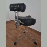 Černá bubenícká židle s polstrováním z umělé kůže a chromovaným kovovým stojanem. Na opěrce hřbetu je bílý nápis 1st CHAIR a pod ním logo TAMA. Na bo…