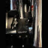 Detailní záběr na černý kovový spojovací prvek značky Gibraltar, který spojuje dvě chromované trubice. Na černé části je bílý nápis Gibraltar. Povrch…