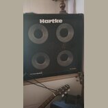 Černý basový kombozesilovač s mřížkou, za kterou jsou vidět čtyři reproduktory. V horní části je bílý nápis Hartke a v pravém dolním rohu označení XL…