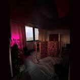 Fotografie zachycuje interiér místnosti s dřevěnou podlahou a kobercem. V prostoru stojí trojdílná akustická clona z dřevěného rámu s červeně vzorova…