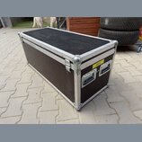Černý transportní flightcase s hliníkovými hranami a kovovými rohy. Na čelní straně jsou dvě madla a žlutý štítek s nápisem BICÍ. Povrch vykazuje běž…