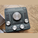 Tmavě šedý audio rozhraní s nápisem AUDIOFUSE Advanced Audio Interface. Zařízení obsahuje několik stříbrných otočných ovladačů s popisky GAIN 1, OUTP…