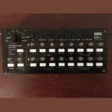Černý sekvencer KORG SQ-1 STEP SEQUENCER s kovovým povrchem. Zařízení obsahuje dvě řady bílých tlačítek, několik ovládacích knofíků a řadu výstupů s…