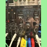 Černý modulární syntetizátor s nápisem WAVES. Na panelu jsou ovládací prvky s popisky FREQUENCY, SLOPE, SMOOTHNESS, SHAPE a SHIFT/LEVEL, dále značení…