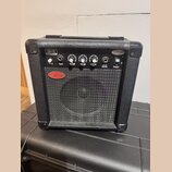 Černý kytarový kombo zesilovač s texturovaným povrchem a kovovou mřížkou reproduktoru. Na ovládacím panelu jsou nápisy CA-15 Guitar Amplifier, Drive,…