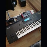 Černý digitální klavír značky YAMAHA s modelem QS30. Nástroj má bílé a černé klávesy, displej a řadu ovládacích tlačítek. Vedle klavíru leží černá sl…