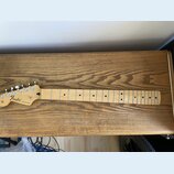Světle hnědý javorový krk elektrické kytary s hmatníkem ze stejného materiálu. Na hlavě je černé logo Fender a nápis STRATOCASTER. Nástroj má stříbrn…