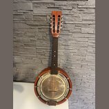 Akustický banjo s hnědým dřevěným tělem a krkem. Instrument má kovový, stříbrný rezonanční povrch s viditelnými šmouhama a oxidací. Na hmatníku jsou…