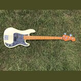 Elektrická basová kytara s krémovým korpusem a hnědým javorovým hmatníkem. Na korpusu je šedý pickguard s texturou mramoru a stříbrný most. Nástroj n…