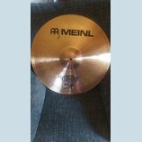 Zlatavý mosazný činel s jemným kruhovým broušením povrchu. Na horní části je černý nápis MEINL a pod ním menším písmem ROLAND MEINL spolu s logem. Ve…