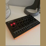 Černý sekvenční syntetizátor s oranžovými bočními panely. Na zařízení je bílý nápis Roland a model T-8, červený digitální displej zobrazující znaki „…