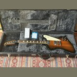 Elektrická kytara s černobrowným přechodem (sunburst) v hnědém tvrdém kufru s šedou vnitřní výplní. Na bílém pickguardu je viditelné logo Gibson. Kyt…