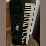 Černý digitální klavír s bílými a černými klávesami. Na levé straně je ovládací panel s displejem, tlačítky a nápisy CASIO a CTK-611. V horní části n…