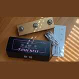 Fotografie zobrazuje zlatý efekt pedál s třemi stoupacími spínači, černou krabici a bílý uživatelský manuál s přiloženým USB kabelem. Na krabici je f…