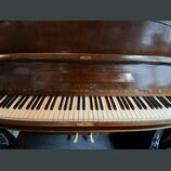 Detail klaviatury a horní části tmavě hnědého dřevěného pianina. Uprostřed nad klávesami je vyryt nápis PETROF. Bílé klávesy vykazují mírné zežlutnut…