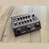 Hnědý kytarový předzesilovač s ovládacími knoflíky a tlačítky. Na přístroji je bílý nápis BOSS a modelové označení Acoustic Preamp AQ-10. Povrch je v…