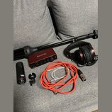 Sada audio vybavení položená na šedém látkovém povrchu. Obsahuje červené zvukové rozhraní s nápisem Focusrite a označením Scarlett 2i2, černý mikrofo…