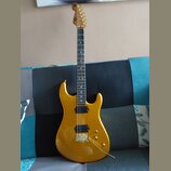 Zlatá elektrická kytara s tvarem superstrat a hnědým hmatníkem. Nástroj má jeden humbucker v pozici mostu, dva snímače typu single-coil a zlatý hardw…