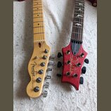 Dvě hlavy elektrických kytar položené vedle sebe na světlém textilu. Levá hlava je z přírodního dřeva s nápisy Fender a TELECASTER®. Pravá hlava je č…