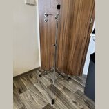 Stříbrný kovový mikrofonní stojan s trojnožkou a rozkládacím mechanismem. Stojan má v horní části držák pro mikrofon a uprostřed regulační šroub. Pov…