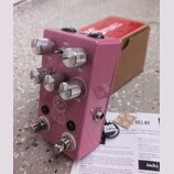 Růžový efekt pedál s kovovým povrchem a čtyřmi stříbrnými ovládacími knoflíky. Na horní části jsou nápisy MOD 2, TIME a MIX, u spodního knoflíku je v…