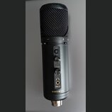 Černý kondenzátorový mikrofon s kovovou síťkou. Na těle jsou nápisy MUTE, GAIN a HEADPHONES u ovládacích prvků, dále označení modelu KM-2U a značka K…