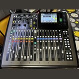 Digitální mixážní pult v černé barvě s řadou posuvníků, tlačítek a ovládacích knoflíků. V horní části je umístěn barevný displej a nápis X32 Compact.…