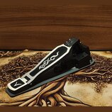 Černý bubenový pedál s hliníkovými stříbrnými prvky. Na horní části pedálu je vyrytý vlnitý ornament a v přední části symbol připomínající stylizovan…