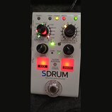 Bílý efekt pedál s nápisy GROOVE, KIT a HATS/RIDES. Na zařízení je vidět velké logo SDRUM a text Strummable Drums™. Obsahuje dva černé otočné knoflík…