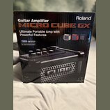 Kartonová krabice s kytarovým zesilovačem. Na povrchu je nápis Roland a model MICRO CUBE GX s textem Ultimate Portable Amp with Powerful Features. Js…