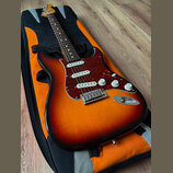 Elektrická kytara typu Stratocaster s barevným přechodem od červené přes oranžovou k žluté a s červeným perleťovým pickguardem. Nástroj má tři bílé s…