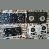 Fotografie zobrazuje čtyři DJ kontrolery položené na vzorité přikrývce. V horní levé části je černý kontroler s nápisy serato a Numark. V horní pravé…