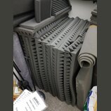 Svrhovatě naskládané šedé akustické pěny s pyramidovitým povrchem. Vedle nich je srolovaný šedý zvukový izolant a další kusy pěnového materiálu. V po…