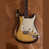 Elektrická kytara s tvarem Stratocaster, trojbarevným sunburst lakem a bílým pickguardem. Tělo vykazuje výrazné opotřebení v podobě rozestřeného laku…