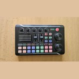 Černý kompaktní zvukový mixér s řadou ovládacích prvků. Na horní části jsou čtyři otočné knoflíky s popisky TREBLE, MID, BASS a RECORD, dva posuvníky…