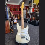 Elektrická kytara typu Stratocaster v krémové barvě s bílým pickguardem a hnedým javorovým hmatníkem. Na hlavě je vidět nápis Fender. Kytara má tři s…