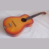 Akustická kytara s žlutě-oranžovým přechodem barvy (sunburst) na deskách a tmavě hnědými boky. Nástroj vykazuje známky opotřebení v podobě škrábanců…