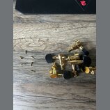 Sada ladíček v zlatém provedení s černými plastovými knoflíky. K ladítkům jsou přiloženy malé zlaté šroubky. Všechny díly leží na dřevěném povrchu.