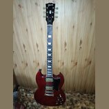 Elektrická kytara typu SG v tmavě červené barvě s černým hmatníkem a černým pickguardem. Na hlavě je bílý nápis Gibson a pod ním označení SG. Nástroj…
