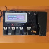 Černý kytarový syntetizátor s nápisem Roland GR-55 GUITAR SYNTHESIZER. Zařízení má digitální displej, na kterém je text LEAD 01-2 Rock Lead Organ, ně…