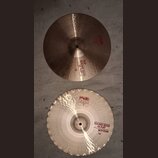 Dvě mosazné činely typu hi-hat o průměru 14". Horní činel nese červené nápisy „PAISTE 2002“ a „TOP SOUND EDGE HI-HAT 14"“. Spodní činel má v horní čá…