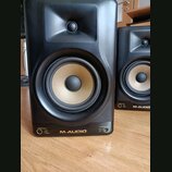 Dva černé studiové monitory s Kevlarovými membránami v béžové barvě. Na spodní hraně je uveden nápis M-AUDIO a vlevo označení SPEAKER MODES s možnost…