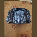 Fotografie znázorňuje malý buben s černobílým mramorovým povrchem a chromovaným kováním. Na korpusu je umístěno kulaté logo s nápisy drums DW, CUSTOM…