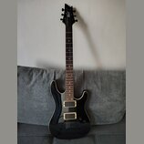 Černá elektrická kytara s bílým lemováním korpusu a hmatníku stehového dřeva. Na hlavě je bílý nápis Cort. Nástroj má konfiguraci dvou humbuckerů a j…
