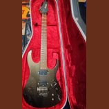 Elektrická kytara s tmavým, kovovým povrchem v červeně vystlaném tvrdém kufru. Na hlavě hmatníku je vidět nápis "ESP". Kytara má dva humbuckery, trem…