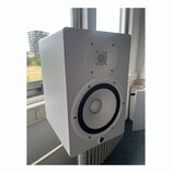 Bílý studiový monitor v hranatém korpusu. Na přední straně jsou dva reproduktory, horní menší s mřížkou a dolní větší s černým okrajem. V pravém doln…