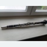 Černý klarinet s kovovými klapkami a stříbrnými kroužky. Nástroj leží v celé délce na světlém povrchu parapetu. Povrch nástroje je hladký a bez vidit…