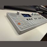 Bílá elektronická klaviatura s kontroléry a displejem. Na ovládacím panelu jsou vidět nápisy JOIN, 1-4 a Shift. Zařízení obsahuje několik bílých tlač…