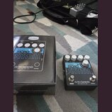 Na fotografii je efekt pedál Bass Mono Synth značky electro-harmonix v černé barvě s bílými nápisy. Vedle pedálu je umístěna jeho originální krabice…