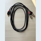 Dva černé audio kabely s konektory typu XLR na jedné straně a RCA na druhé. Na kabelích je vidět bílý nápis AUDIO CABLE a MODEL. Konektory RCA jsou v…
